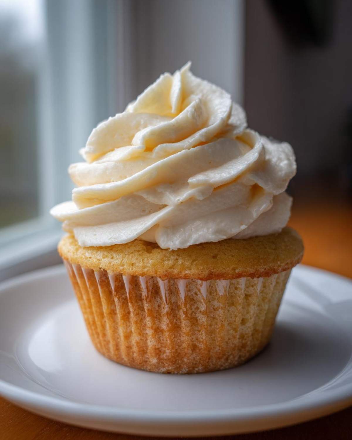 A single, perfectly baked vanilla cupcakes topped with a generous swirl of creamy white vanilla frosting.