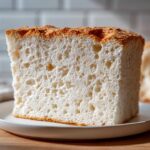Close-up of a tall, square slice of angel food cake showing its airy, white crumb structure.