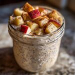 Close-up of apple cinnamon overnight oats in a glass jar, topped with diced apples and cinnamon.