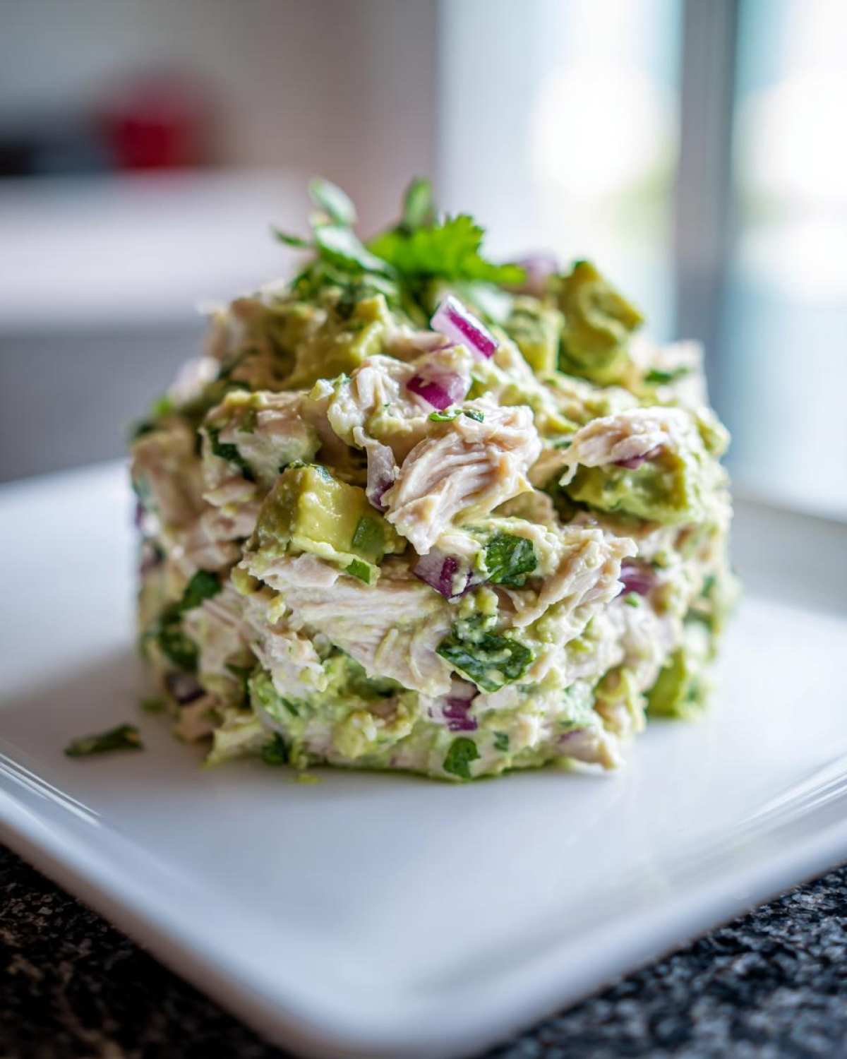 A molded serving of creamy avocado chicken salad topped with fresh cilantro on a white square plate.