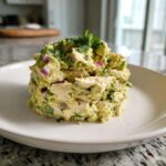 A perfectly molded serving of creamy avocado chicken salad mixed with red onion and topped with fresh cilantro.