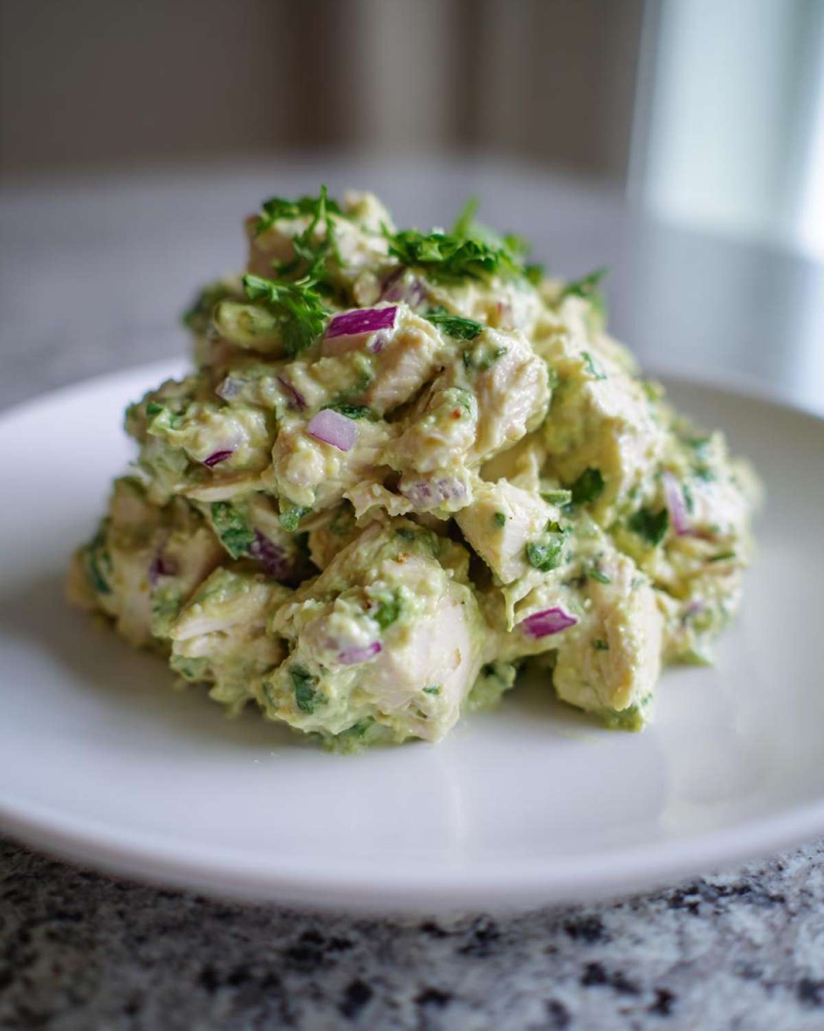 A mound of creamy avocado chicken salad mixed with visible chunks of red onion, served on a white plate.