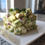 A mound of fresh avocado chicken salad featuring chunks of avocado, chicken, and red onion, garnished with cilantro.
