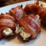 Close-up of crispy bacon wrapped stuffed dates filled with creamy cheese on a white plate.