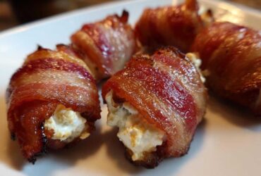 Close-up of crispy bacon wrapped stuffed dates filled with creamy cheese on a white plate.