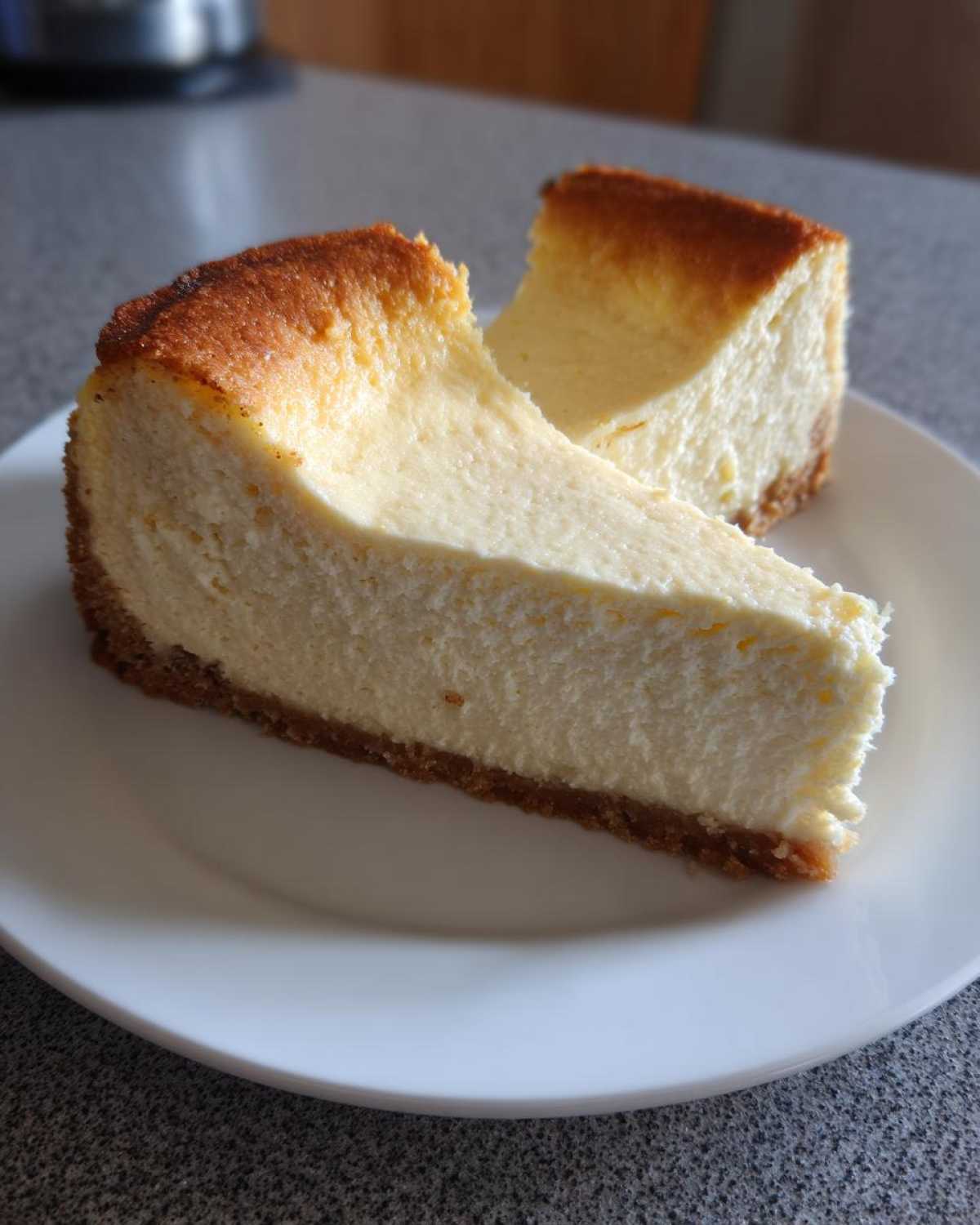 Two slices of creamy, baked Protein Cheesecake with a golden-brown top and graham cracker crust served on a white plate.