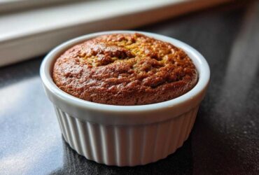 Close-up of a golden brown banana protein muffin baked in a white, fluted ramekin.