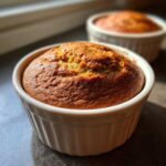 Close-up of a golden brown banana protein muffins baked individually in a white ramekin dish.