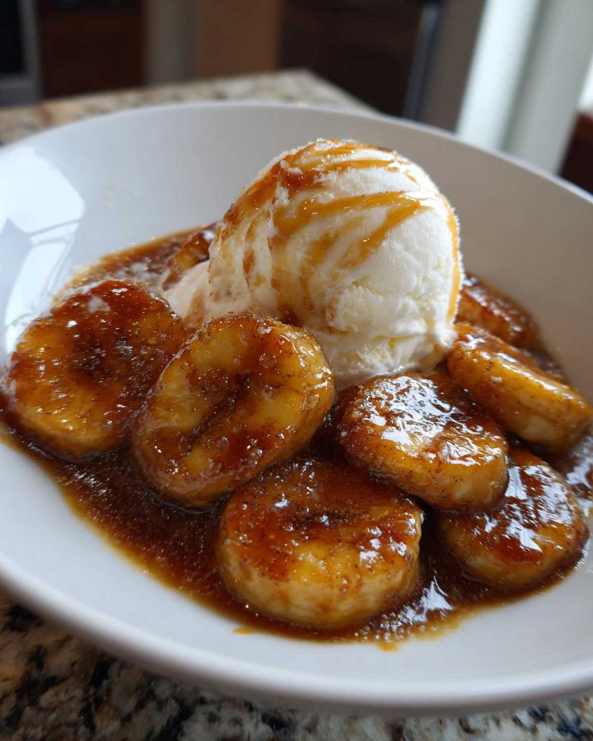 A white bowl filled with caramelized bananas in rich sauce and a scoop of vanilla ice cream, representing delicious bananas foster.