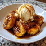 Close-up of caramelized bananas foster topped with a scoop of vanilla ice cream and caramel drizzle.