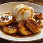 A serving of caramelized bananas foster topped with a scoop of vanilla ice cream and drizzled with warm sauce.