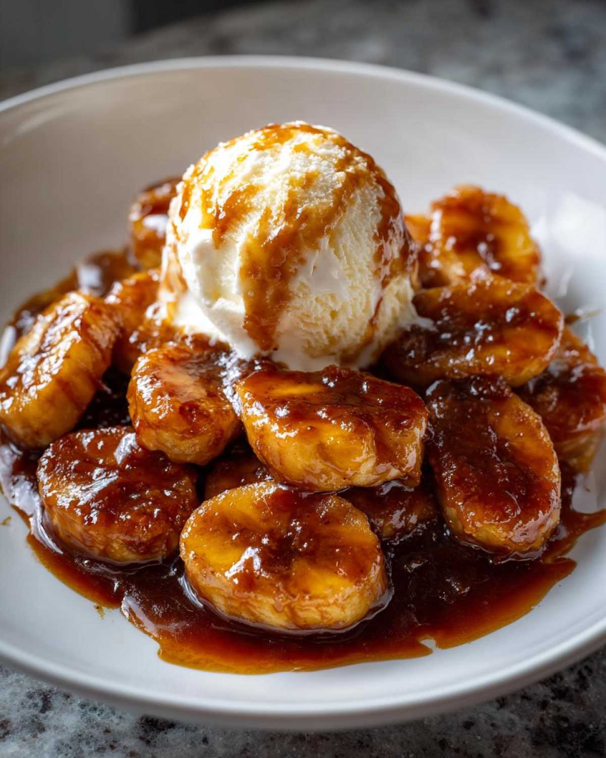 Close-up of caramelized bananas in rich sauce topped with vanilla ice cream, classic Bananas Foster.