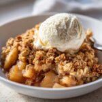 Close-up of a serving of the best apple crisp recipe, featuring warm, spiced apples and a crunchy oat topping crowned with vanilla ice cream.
