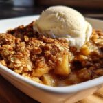 Close-up of a warm apple crisp recipe serving topped with a scoop of vanilla ice cream in a white bowl.