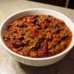 Close-up of a white bowl filled with rich, thick chili featuring ground meat and kidney beans, showcasing the best chili recipe.