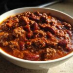 Close-up of a hearty bowl of chili featuring ground beef and kidney beans in a rich, dark red sauce, perfect for the best chili recipe.