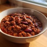 Close-up of a steaming bowl containing the best chili recipe, rich with ground meat and kidney beans.