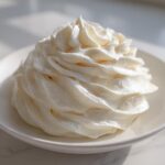A beautiful, tall swirl of fluffy white cream cheese frosting piped onto a small white dish.