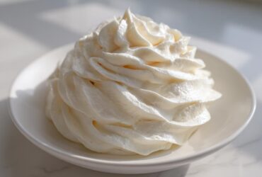A beautiful, tall swirl of fluffy white cream cheese frosting piped onto a small white dish.