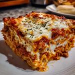 A thick, delicious slice of homemade lasagna showing layers of pasta, meat sauce, and melted cheese, sprinkled with herbs.