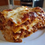 A thick, layered slice of homemade lasagna featuring rich meat sauce and melted cheese on a white plate.
