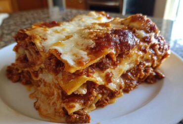 A thick, layered slice of homemade lasagna featuring rich meat sauce and melted cheese on a white plate.