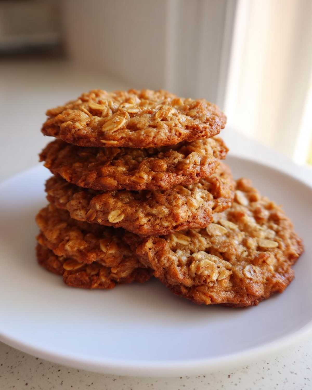 A stack of five golden brown, chewy oatmeal cookie rounds resting on a white plate.