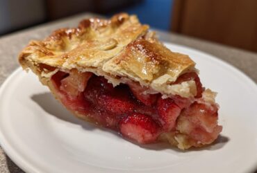 A close-up of a juicy slice of strawberry rhubarb pie showing the bright red filling and golden, flaky top crust.