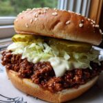 A fully assembled big mac sloppy joes sandwich featuring a sesame seed bun, savory meat sauce, shredded lettuce, pickles, and special sauce.