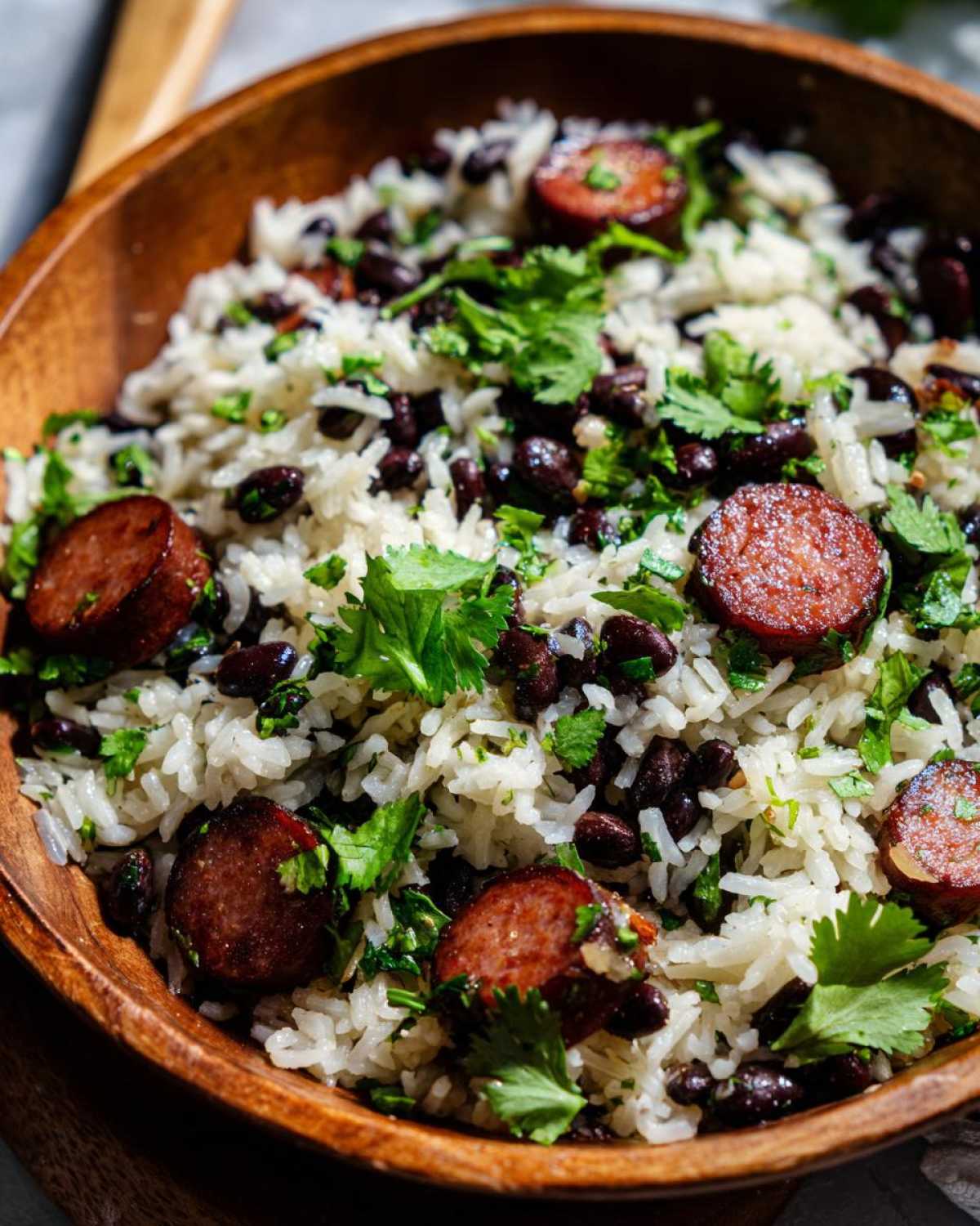 Close-up of flavorful black beans and rice mixed with sliced smoked sausage and fresh cilantro.