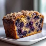 A moist slice of blueberry banana bread featuring visible blueberries and a crunchy cinnamon sugar streusel topping.