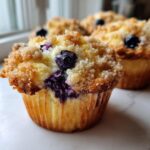 Close-up of a delicious blueberry muffin featuring a golden crumb topping and visible burst blueberries.