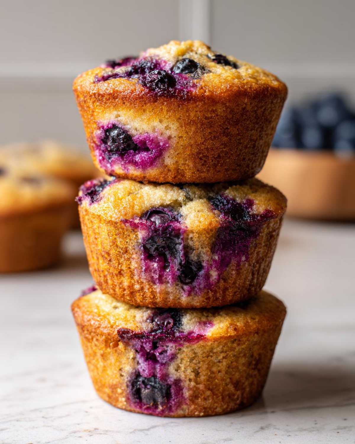 Close-up of three stacked blueberry protein muffins with golden tops and vibrant purple berry bursts.