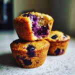 Close-up of two stacked blueberry protein muffins, one with a bite taken out revealing the moist interior.