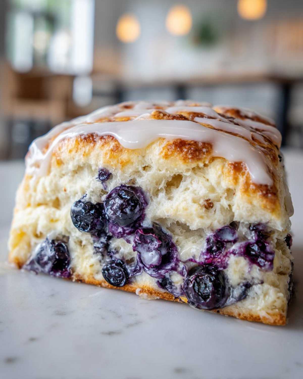 A close-up cross-section of a freshly baked blueberry scone, generously studded with juicy blueberries and topped with white glaze.