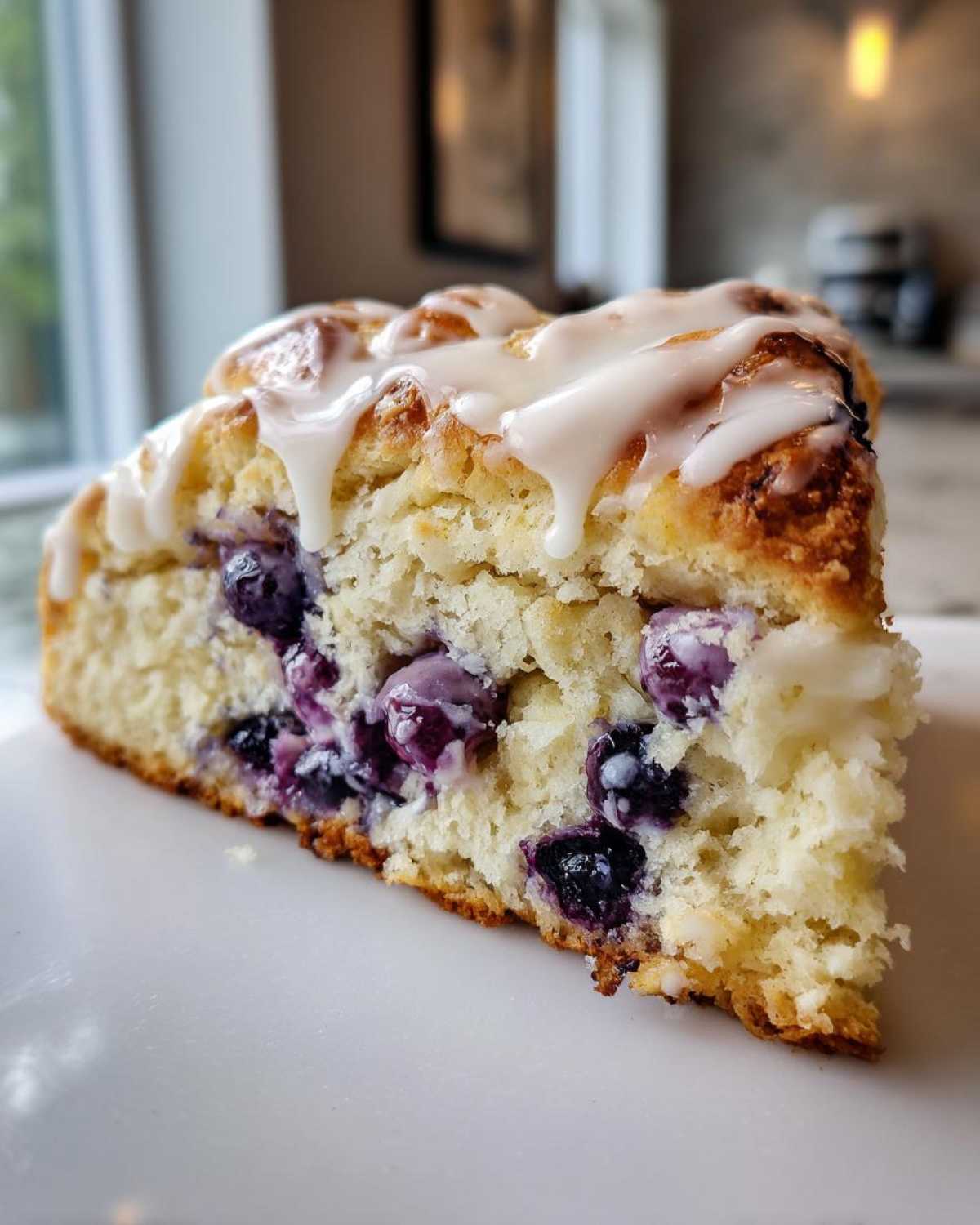 A close-up, cross-section view of a fluffy blueberry scones slice topped with a sweet white glaze.