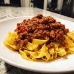 A generous serving of rich bolognese sauce piled high on a nest of fresh fettuccine pasta.