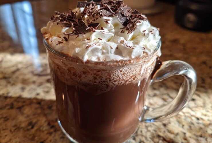 A clear glass mug filled with rich boozy hot chocolate, topped with whipped cream and chocolate shavings.