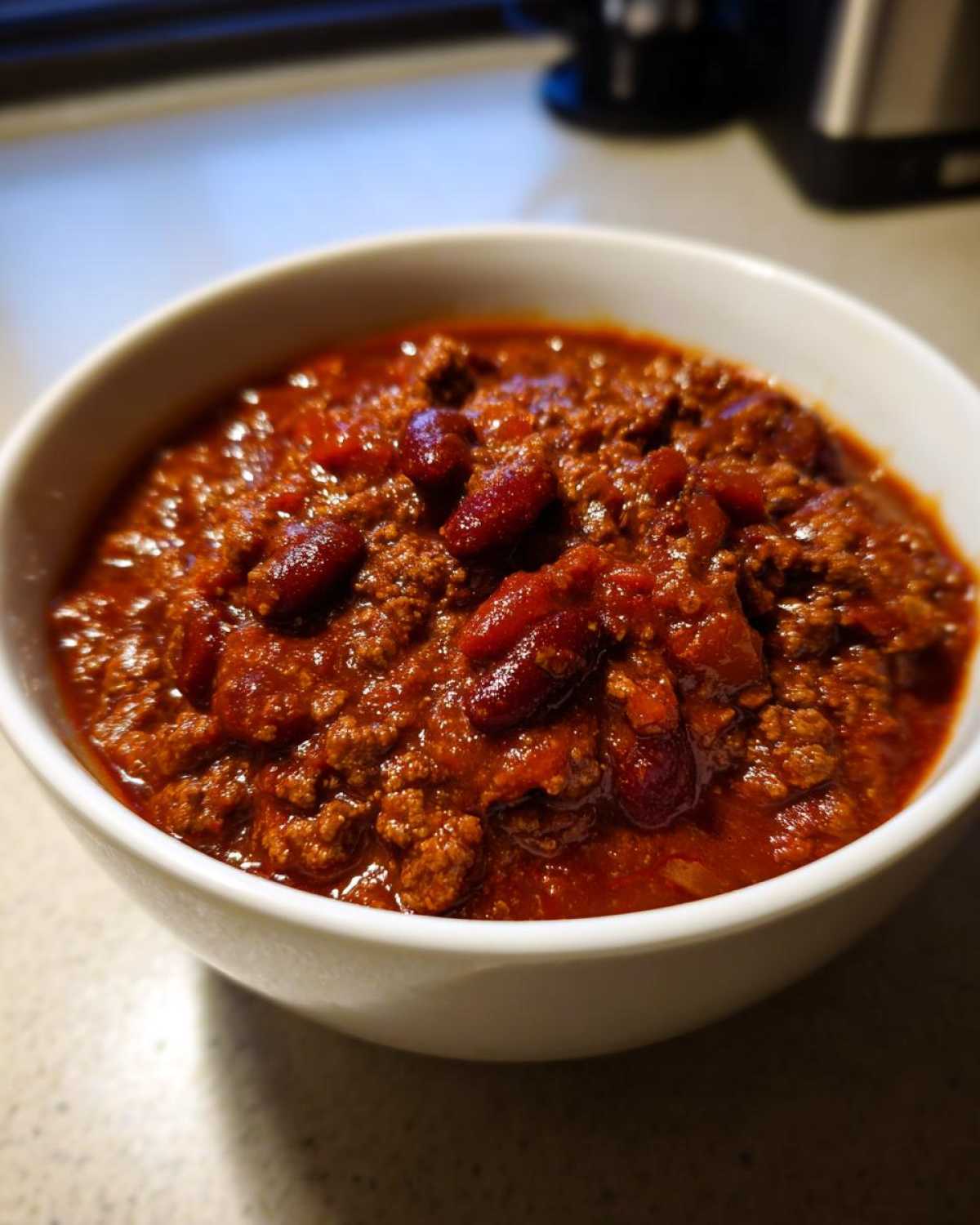 Close-up of a hearty bowl of thick, dark red chili with ground meat and kidney beans, representing the best chili recipe.