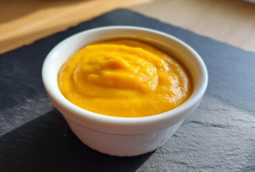 Close-up of thick, bright orange nacho cheese sauce served in a small white dipping bowl on a dark slate surface.
