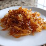 A close-up of a pile of rich, golden brown caramelized onions served on a white plate.