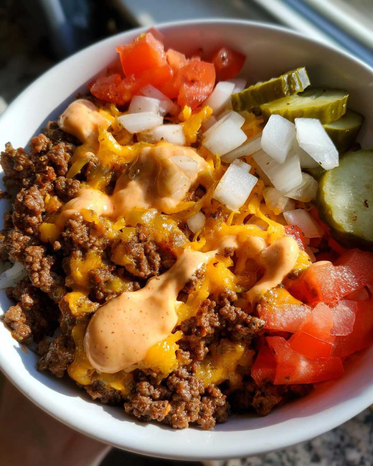 Close-up of a delicious cheeseburger bowl featuring seasoned ground beef, melted cheddar, special sauce, diced onions, tomatoes, and pickles.