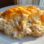 A close-up serving of cheesy chicken and rice casserole topped with melted, golden cheddar cheese.