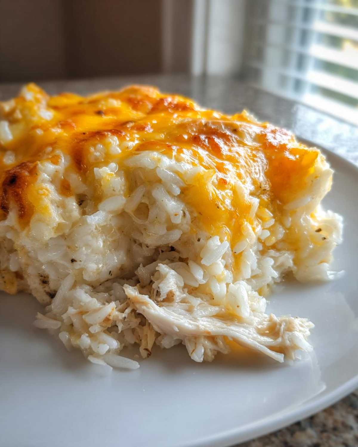A close-up of a serving of cheesy chicken and rice casserole with melted cheddar cheese on top.