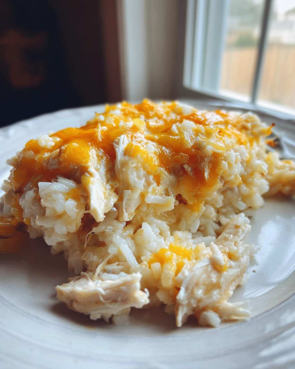 Close-up of a serving of cheesy chicken and rice, topped with melted cheddar cheese.