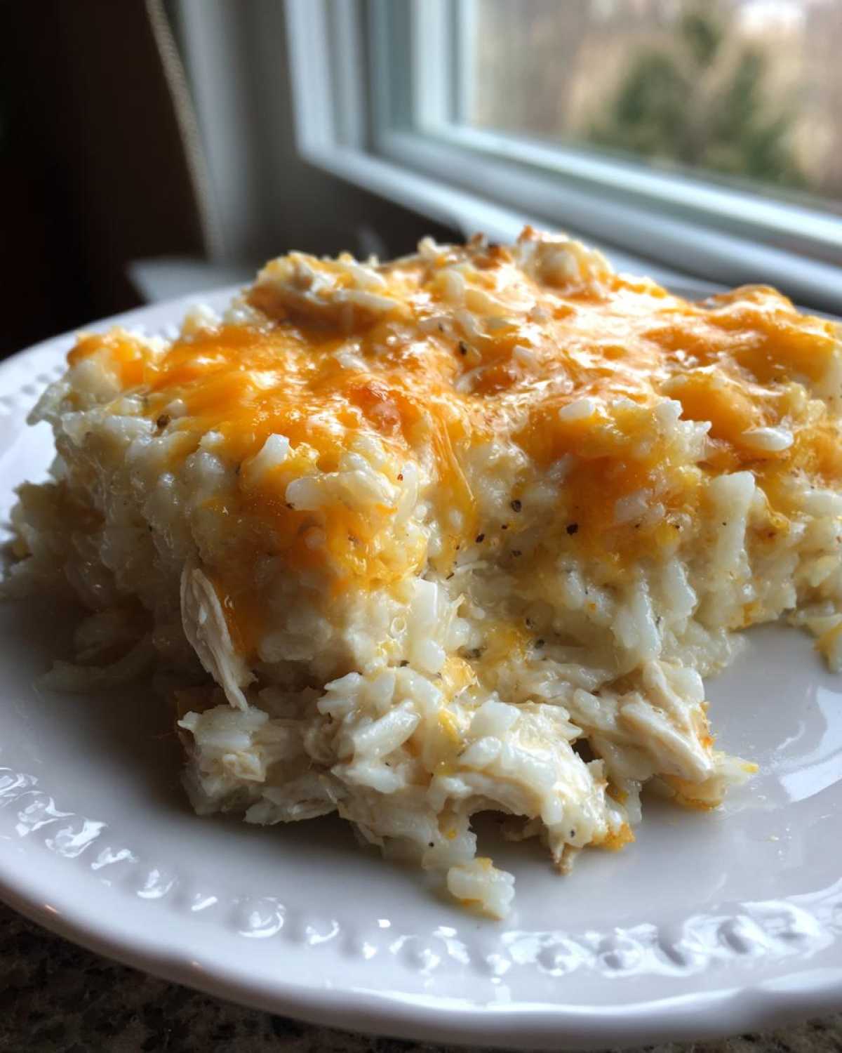 A close-up of a serving of cheesy chicken and rice casserole topped with melted cheddar cheese.