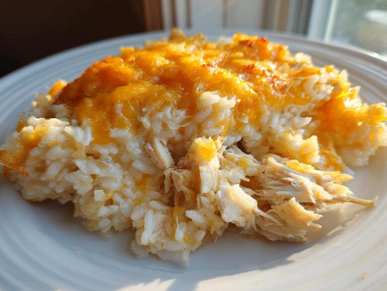 A close-up serving of cheesy chicken and rice casserole topped with melted, golden cheddar cheese.
