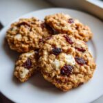 Close-up of several chewy cranberry oatmeal cookies with white chocolate chunks on a white plate.