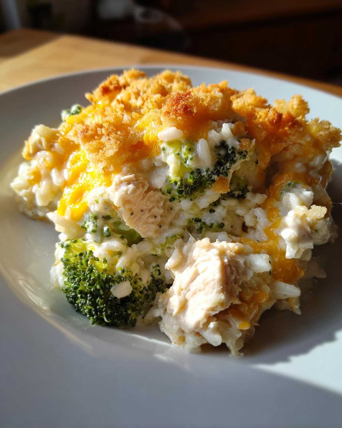 A close-up serving of creamy chicken broccoli rice casserole topped with melted cheese and a golden, crunchy breadcrumb topping.