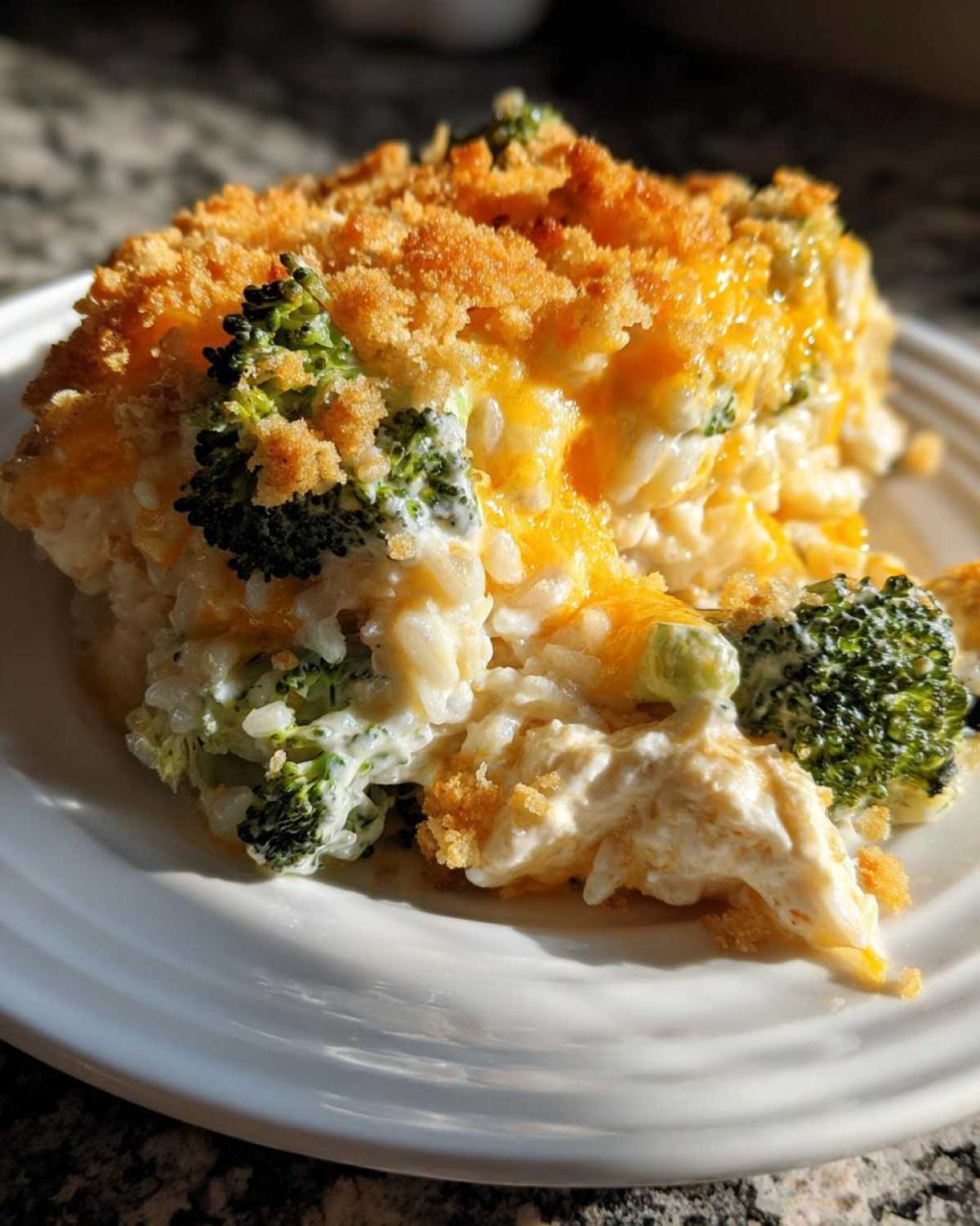 A close-up serving of creamy chicken broccoli rice casserole topped with melted cheddar cheese and golden breadcrumbs.